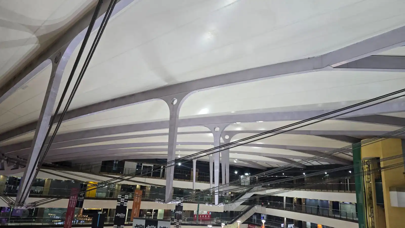 Vasant Square Mall Vasant Kunj — the daylit-by-night court seen from a balustrade, membrane roof above the glazed lift and escalators, Ekra Decor